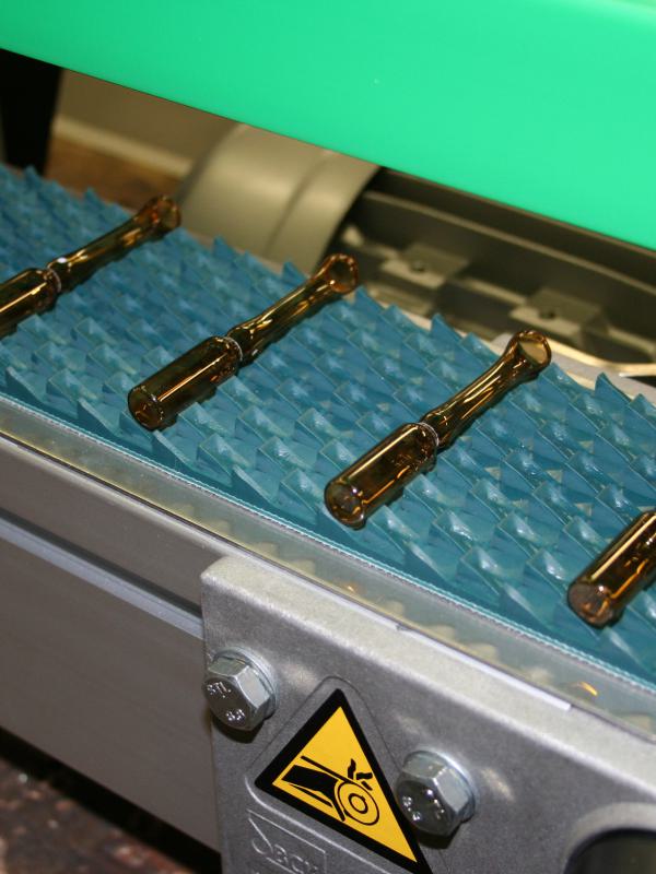 Transport of ampoules on a saw-tooth belt material.